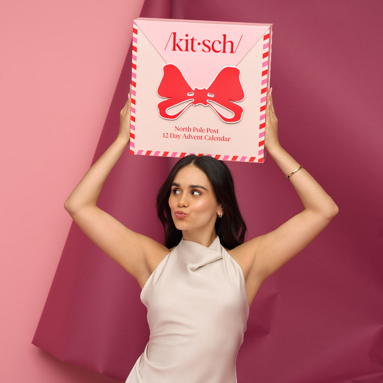 Woman holding a 'kit-sch' Advent calendar against a pink background