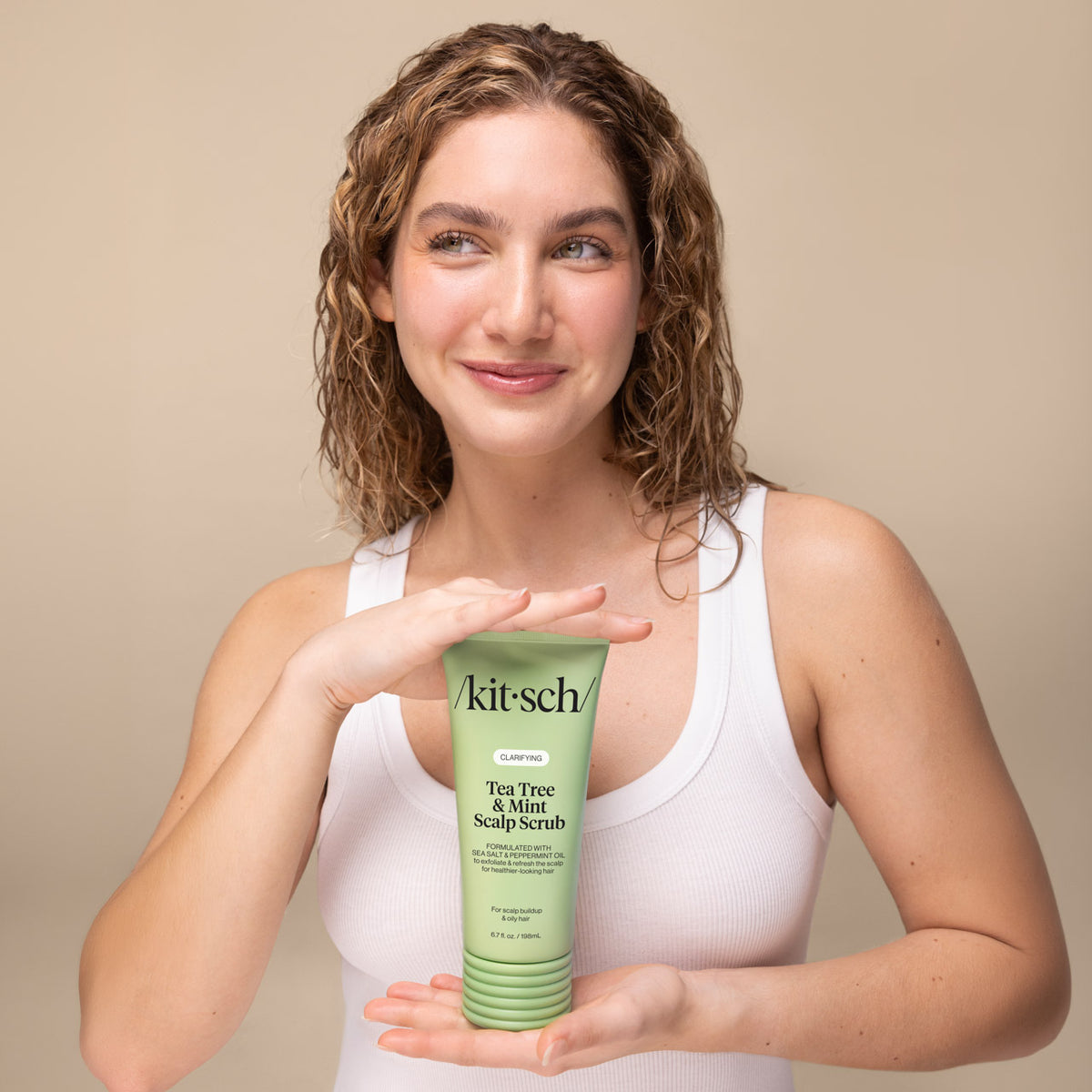 KITSCH Clarifying Tea Tree & Mint Scalp Scrub — model with damp curly hair holding the green scalp scrub tube between her hands — Cooling, minty sensation turns your routine into a refreshing shower ritual — wash day