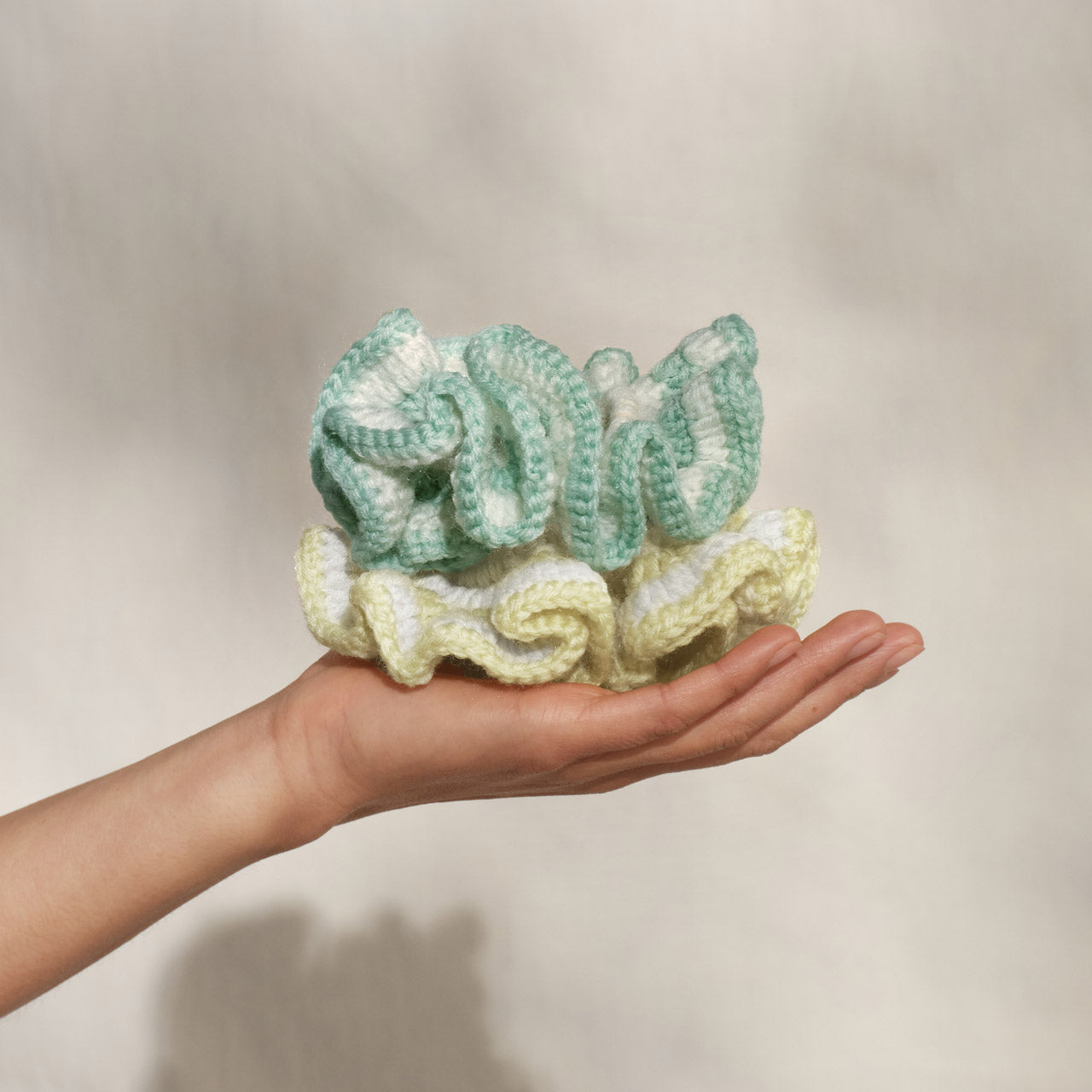 Hand holding Kitsch Coastal Cottage Crochet Scrunchies in seafoam blue and butter yellow 