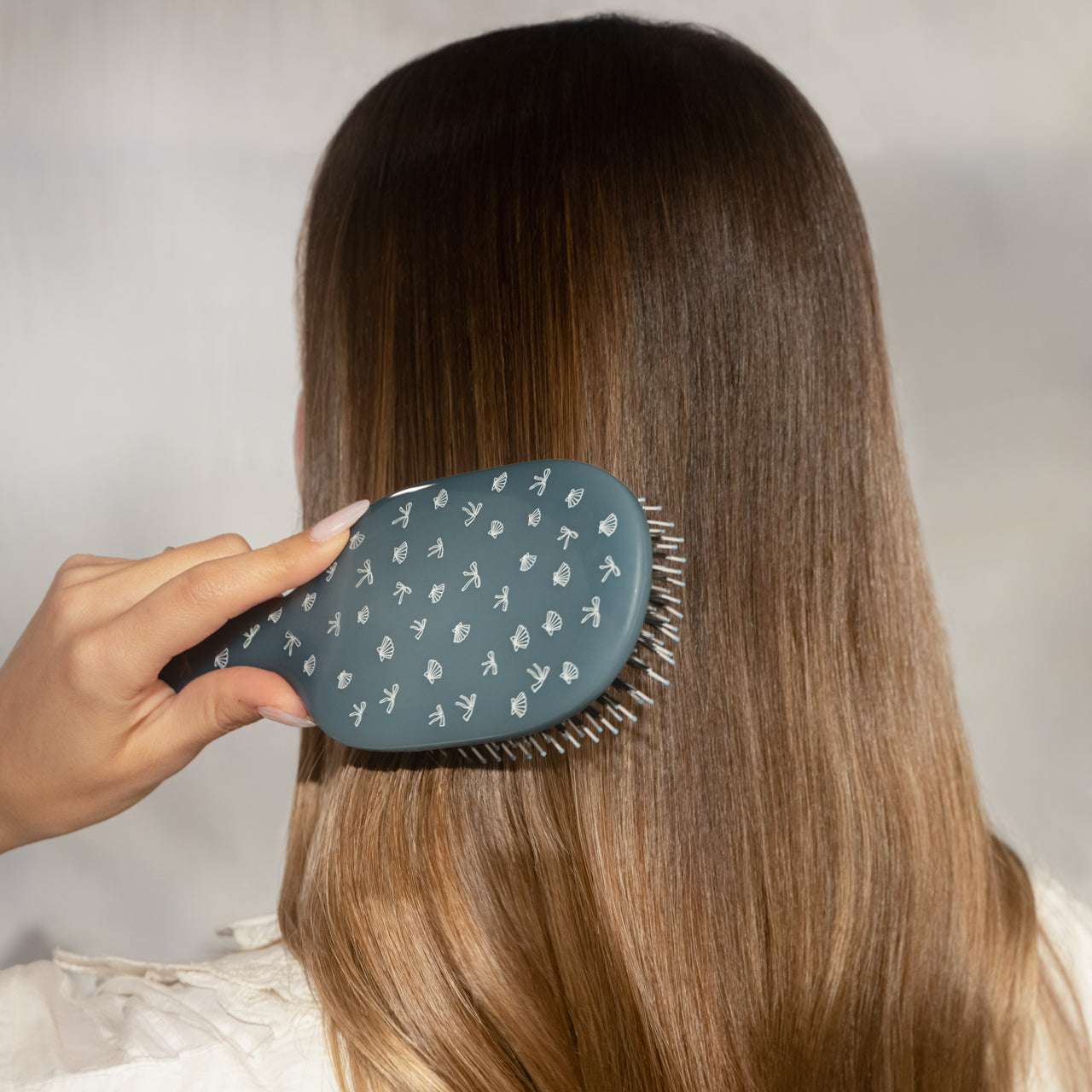 Model brushing long straight hair with Kitsch Coastal Blue Print Smooth & Polish Brush – frizz-free finish