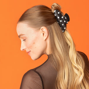 Model wearing the Recycled Plastic Glitter Claw Clip in Ghosts, styling a half-up hairstyle with a black glitter ghost-print claw clip.