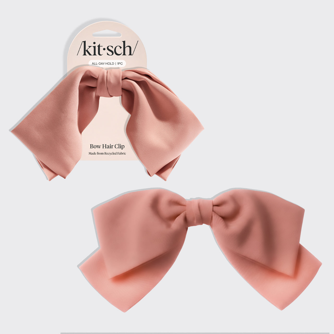 A dusty pink satin bow hair clip shown both on its white retail card packaging and as a standalone product against a light gray background. The brand name 'kitsch' is clearly visible on the header card.