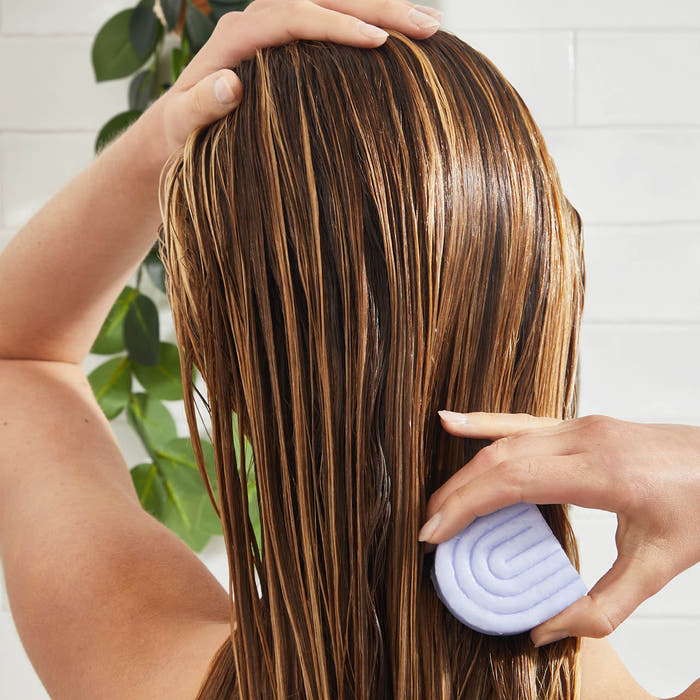 Woman applying KITSCH Purple Toning + Biotin Solid Conditioner Bar to highlighted hair in the bathroom — sulfate-free, paraben-free, silicone-free toning conditioner bar that neutralizes brassiness, boosts shine with Biotin, and deeply conditions color-treated and highlighted hair